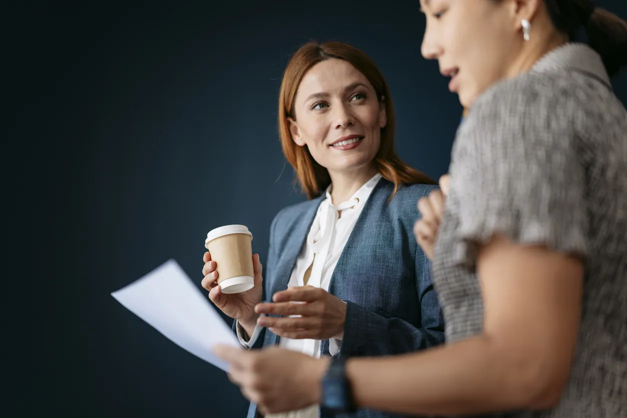 Deux femmes dans la trentaine consultent un document ensemble, café à la main